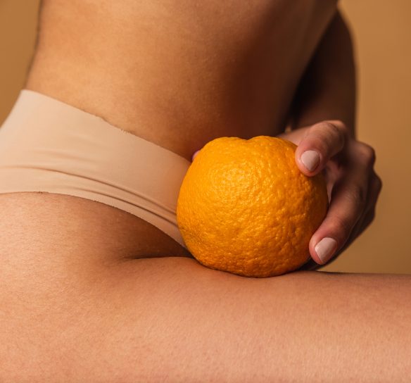 Femme en sous vêtement beige, peau lisse et ferme, tenant dans sa main une orange - Dimpless